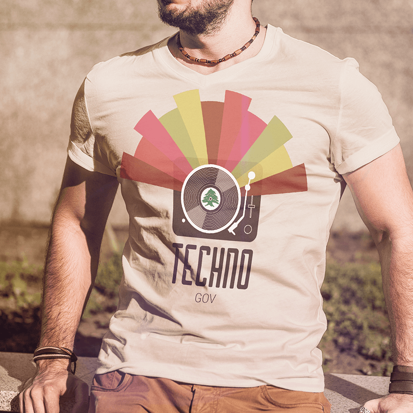 A beige t-shirt with text saying 'techno-gov' with an illustration of a DJ's mixer and technicolors radiating out of it.